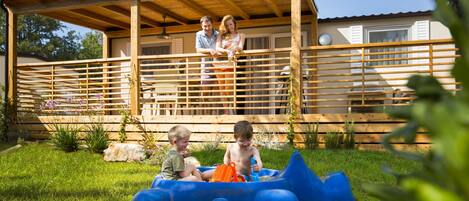 A wooden deck with a railing, a covered area, and a house in the background.