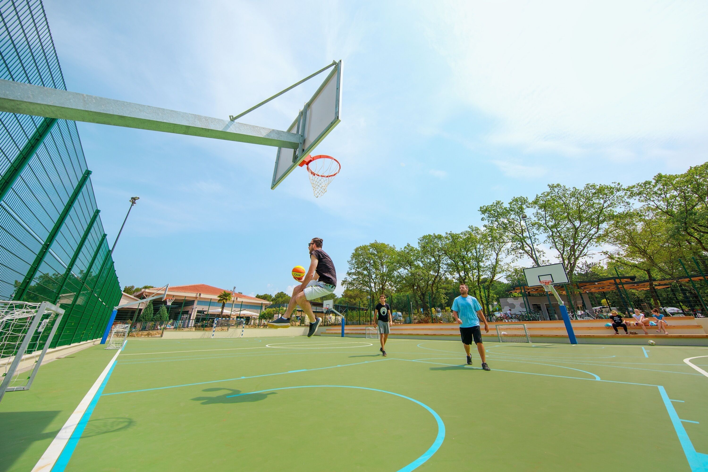 An outdoor basketball court with a hoop, a net, and a basketball in mid-air.
