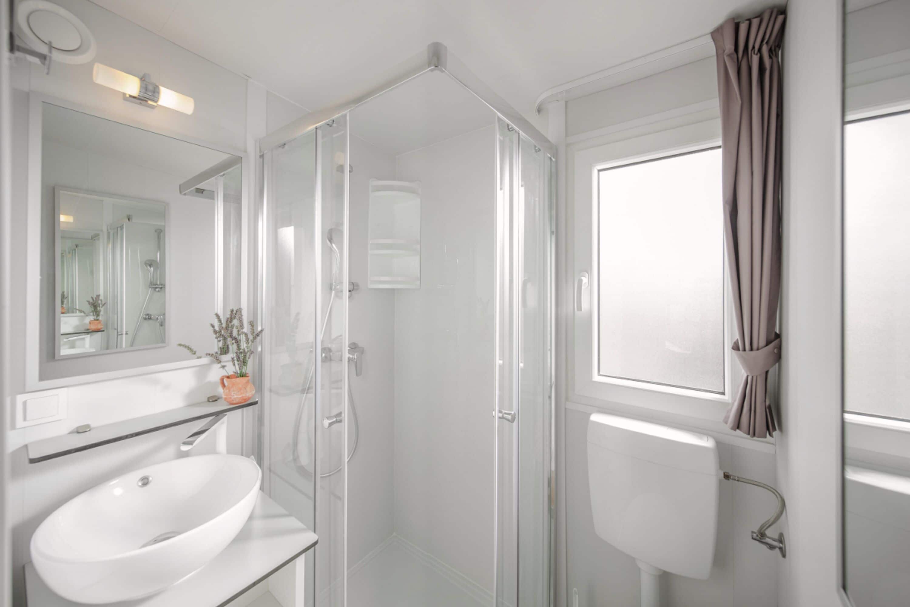 A modern bathroom with a glass-enclosed shower, a white sink, and a large mirror.