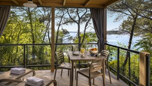 A balcony with a table set for two, overlooking a body of water and trees. - Valamar Camping Lanterna (Tar-Vabriga)
