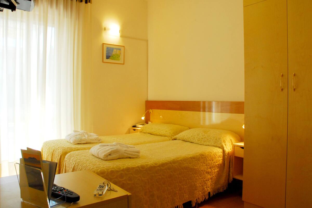 A hotel room with two beds, a desk with a laptop, a remote control, and a telephone.