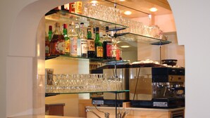 A bar area with shelves of liquor bottles and glasses, a coffee machine, and a sign indicating a protected local business. - Grazia Hotel (Sperlonga)