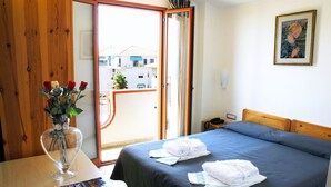 A hotel room with a bed, a wooden desk, a vase with flowers, and a view of buildings outside. - Grazia Hotel (Sperlonga)