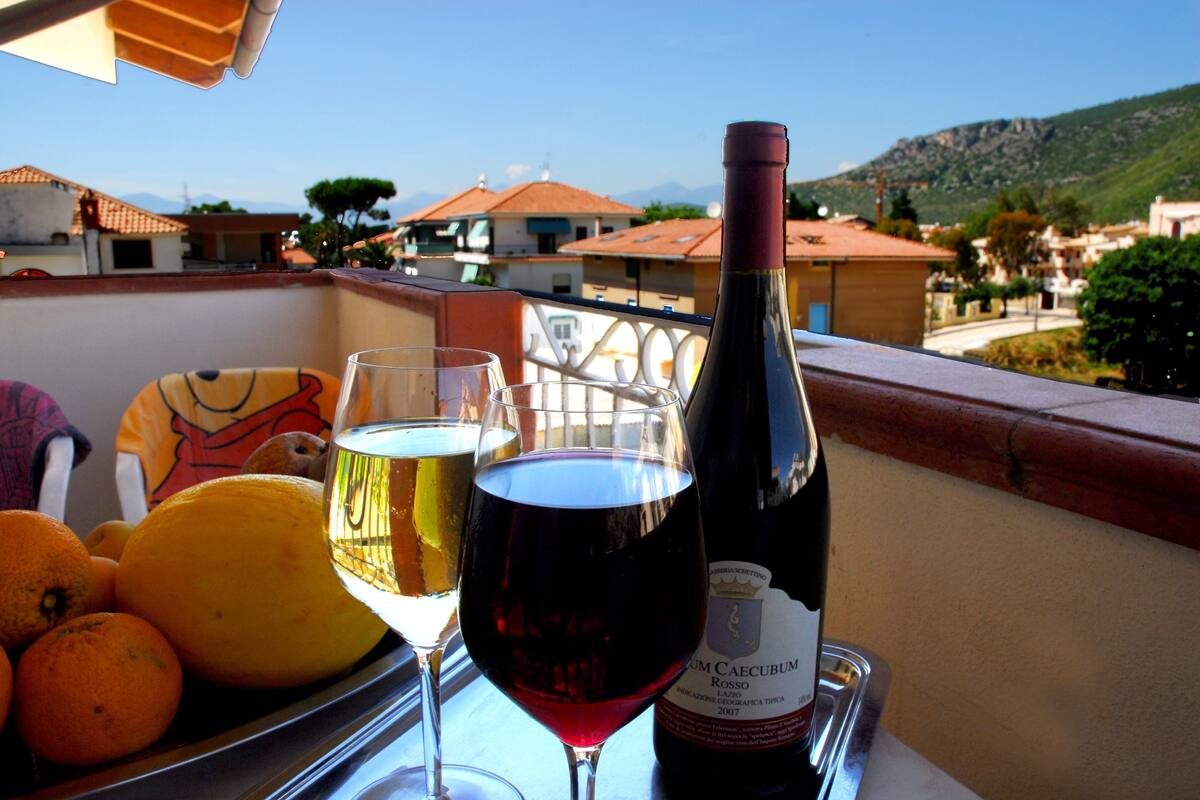 A balcony with a table holding a wine bottle, glasses, and oranges.