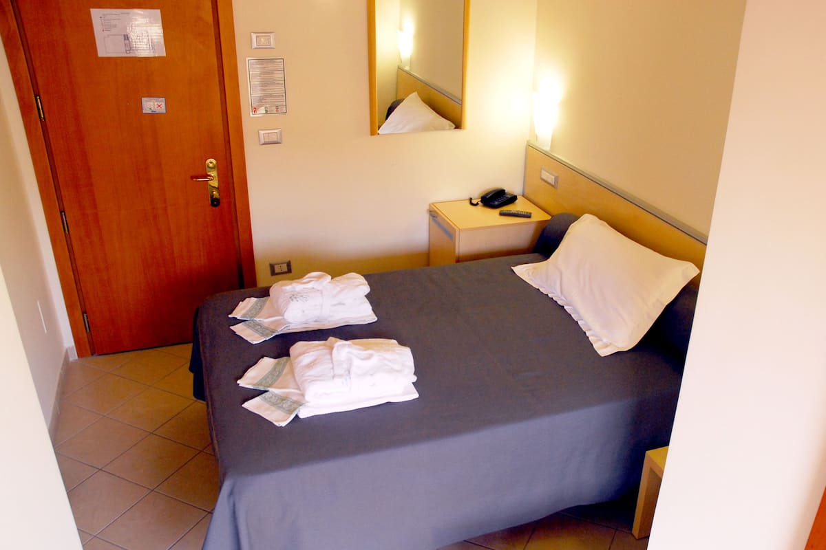 A hotel room with a bed, a bedside table with a phone, a mirror, and a door.