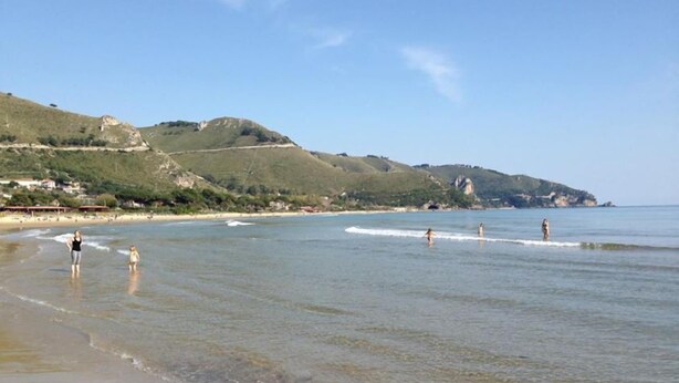 A beach with clear water, people in the water, and hills in the background. - Grazia Hotel (Sperlonga)