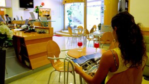 A woman reading a magazine at a table in a cafe with yellow chairs and a wooden counter. - Grazia Hotel (Sperlonga)