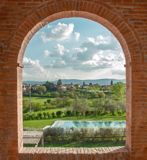 Una estructura de ladrillo en arco con vistas a una piscina, vegetación y edificios a la distancia.