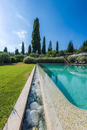 A swimming pool with a pebble-lined edge, surrounded by a grassy lawn and trees. - Relais la Leopoldina (Sinalunga)
