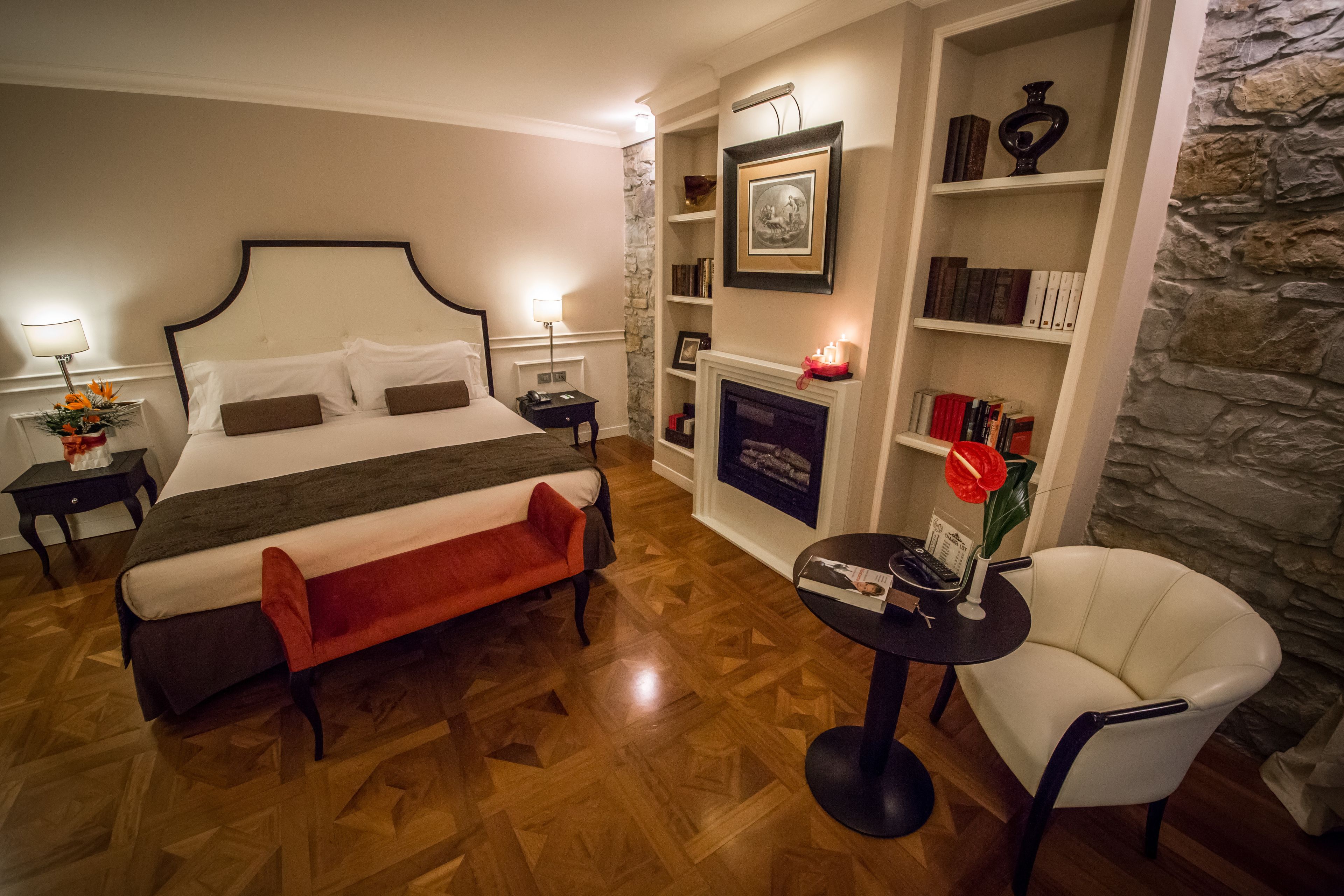 Habitación de hotel con una cama grande, una mesita con una silla, una estantería y una chimenea.