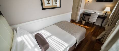 A hotel room with a bed, a desk, a chair, a TV, and framed artwork on the wall.
