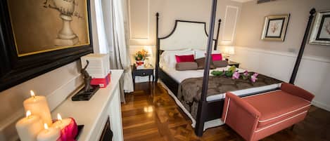 A four-poster bed with a headboard, a bedside table with a lamp, a small table with a vase of flowers, and a red bench.