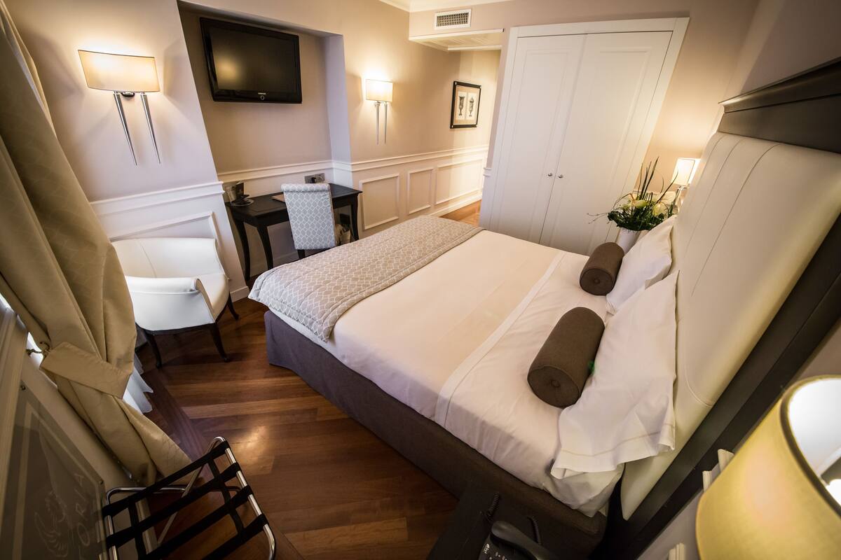 A hotel room with a bed, bedside table, chair, TV, and a door.