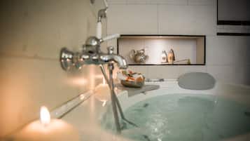 Une salle de bain avec une baignoire, une bougie allumée et une étagère ornée d’objets décoratifs.