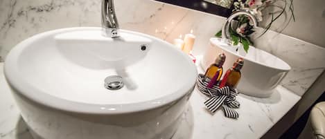 A bathroom sink with a marble countertop, a mirror, and a vase with flowers.