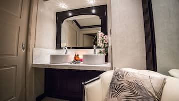 A bathroom with a double sink, a large mirror, and a decorative pillow on a chair.
