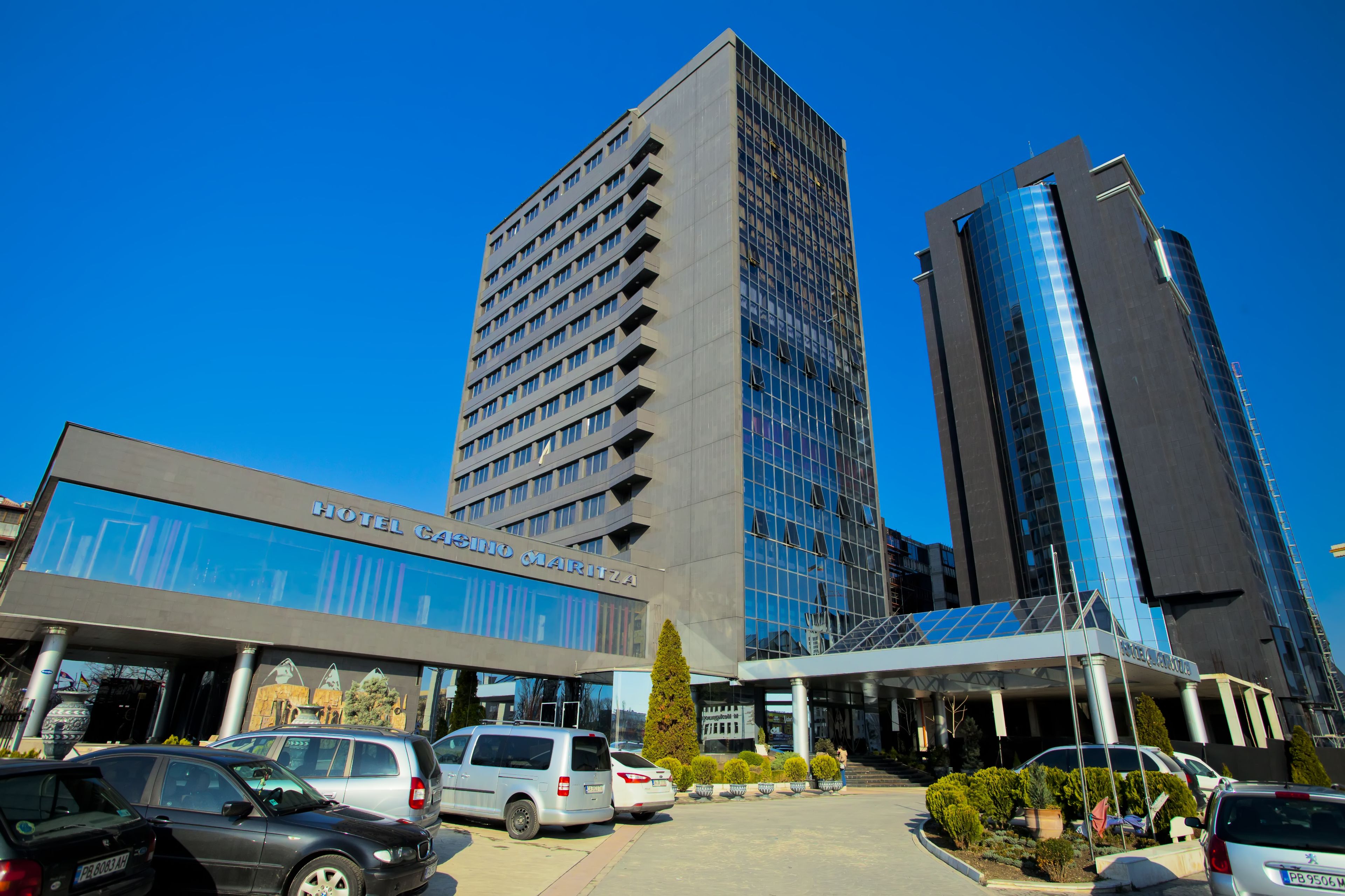 A hotel with a modern facade, a prominent entrance, and a parking area with several vehicles.