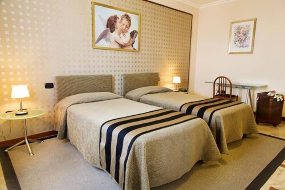A hotel room with two beds, a small table, a chair, and a desk.