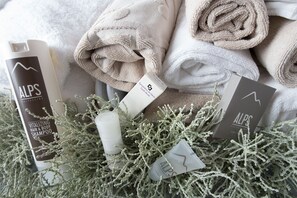 A collection of ALPS brand toiletries, including a shampoo bottle, a bar of soap, and a facial cleanser, alongside neatly folded towels. - Vedig (Valfurva)