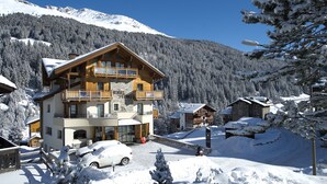A multi-story wooden lodge with balconies, a ski lift, and a snowy mountain backdrop. - Vedig (Valfurva)