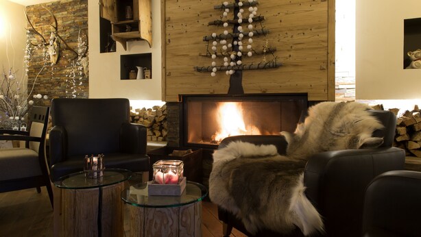 A cozy living room with a fireplace, a wooden wall decoration, and a glass coffee table with a candle. - Vedig (Valfurva)