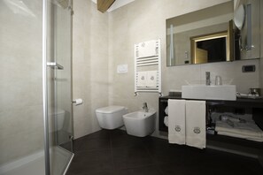 Ein modernes Badezimmer mit Duschkabine aus Glas, einem Bidet, einem Waschbecken und einem Spiegel mit goldener Rahmung.