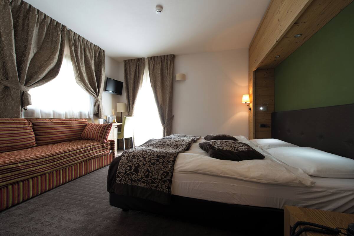 Una habitación de hotel con cama, sofá, televisor y lámpara.