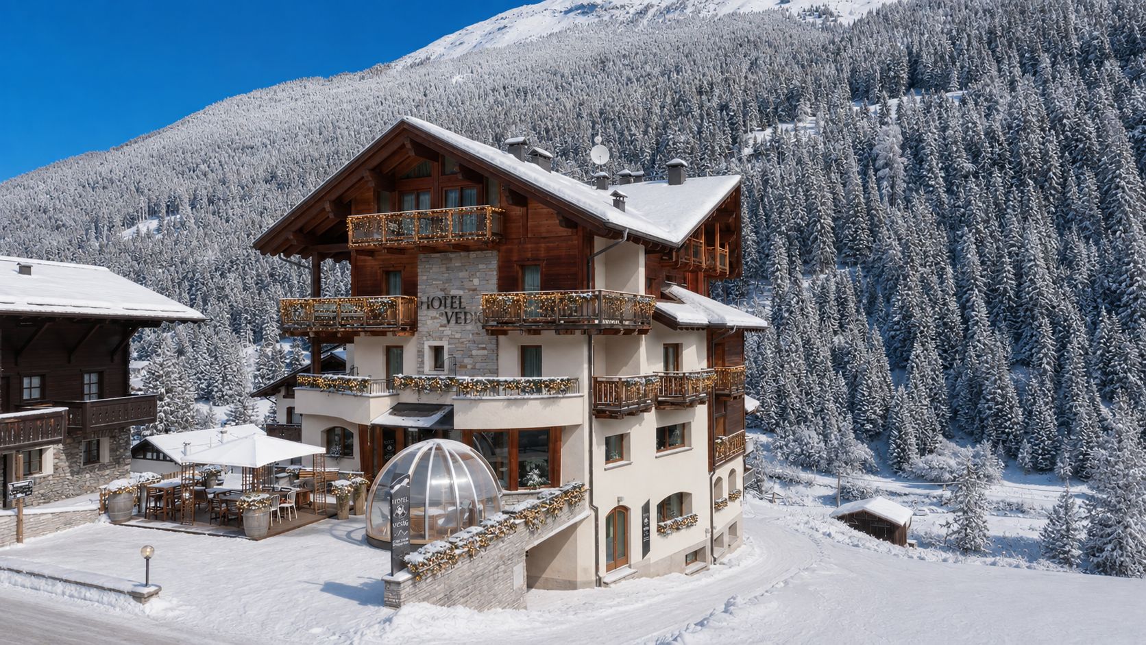 A multi-story hotel with balconies, a covered outdoor seating area, and a snow-covered mountain backdrop.