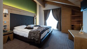A bedroom with a bed, bedside tables, a TV, and a window with curtains. - Vedig (Valfurva)