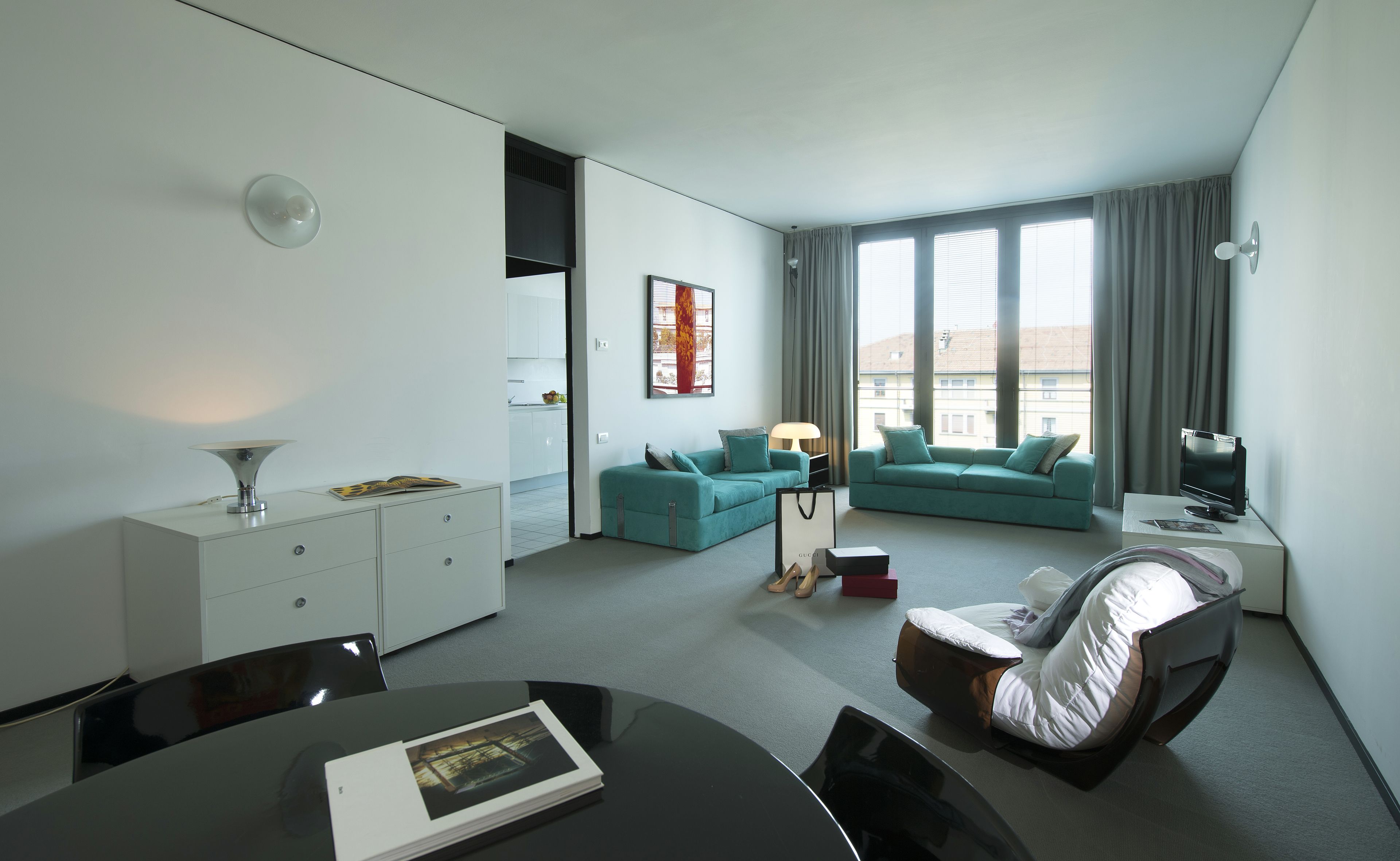 A modern hotel room with a dining area, a sofa, a chair, a TV, and a window with curtains.