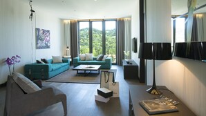 Una sala de estar moderna con un sofá, una mesa de centro y un televisor. Hay un ventanal con cortinas, un cuadro en la pared y una lámpara de pie.