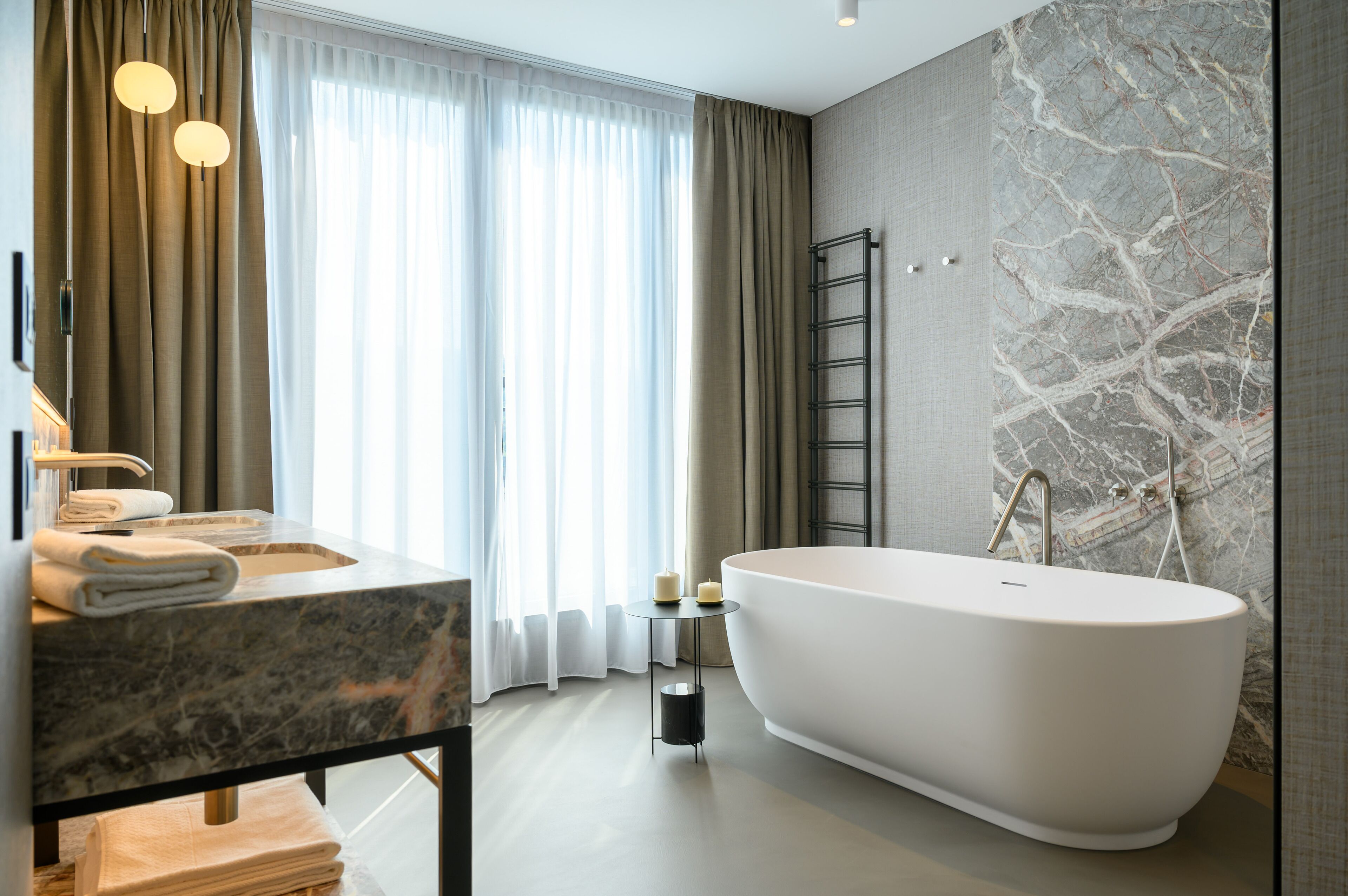 Un baño moderno con una bañera independiente, un lavabo de mármol y un ventanal con cortinas de gasa.