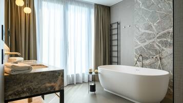 Un baño moderno con una bañera independiente, un lavabo de mármol y un ventanal con cortinas de gasa.