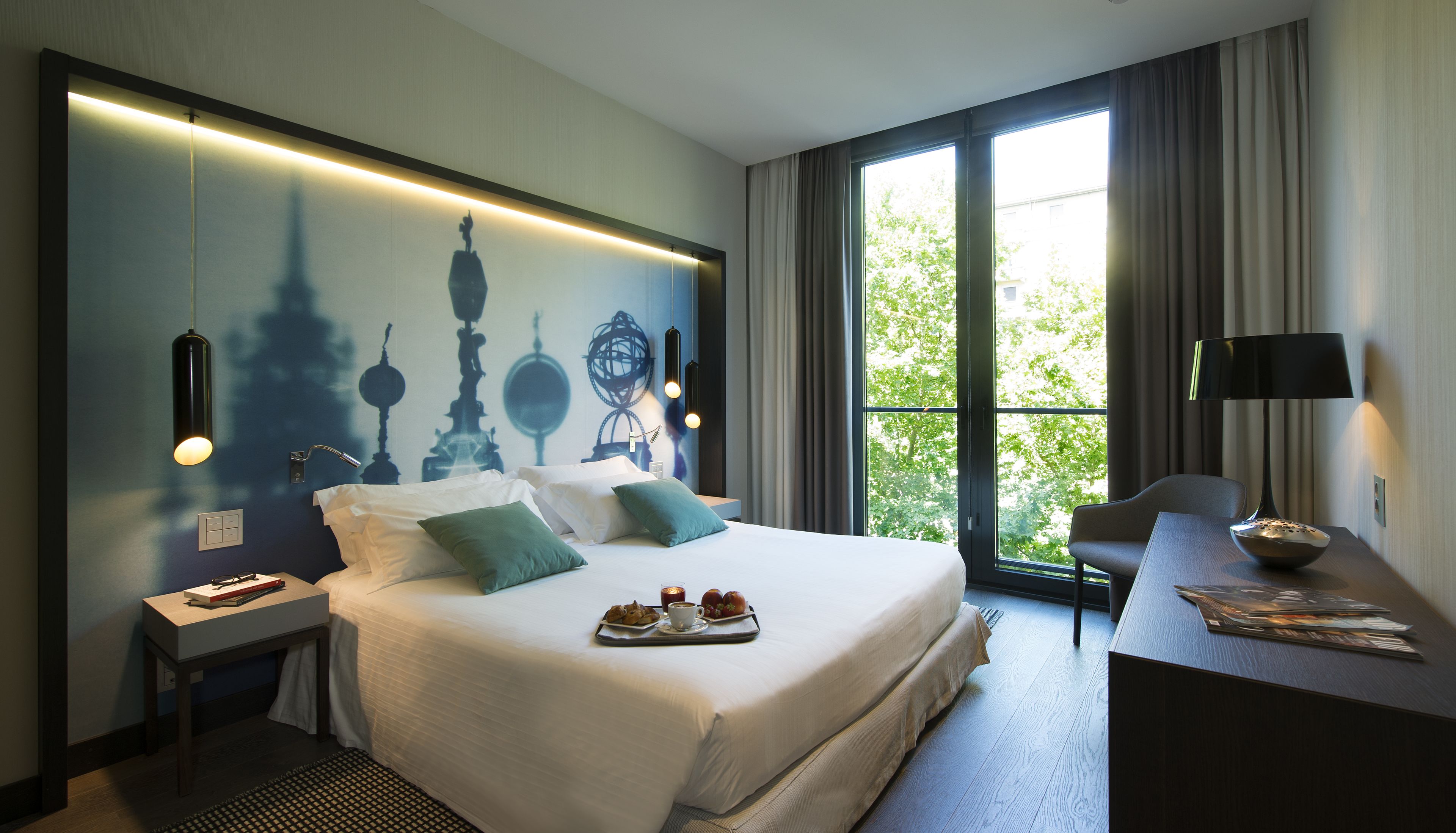 Ein modernes Hotelzimmer mit einem großen Bett, einem Schreibtisch und Blick auf Bäume durch das Fenster.