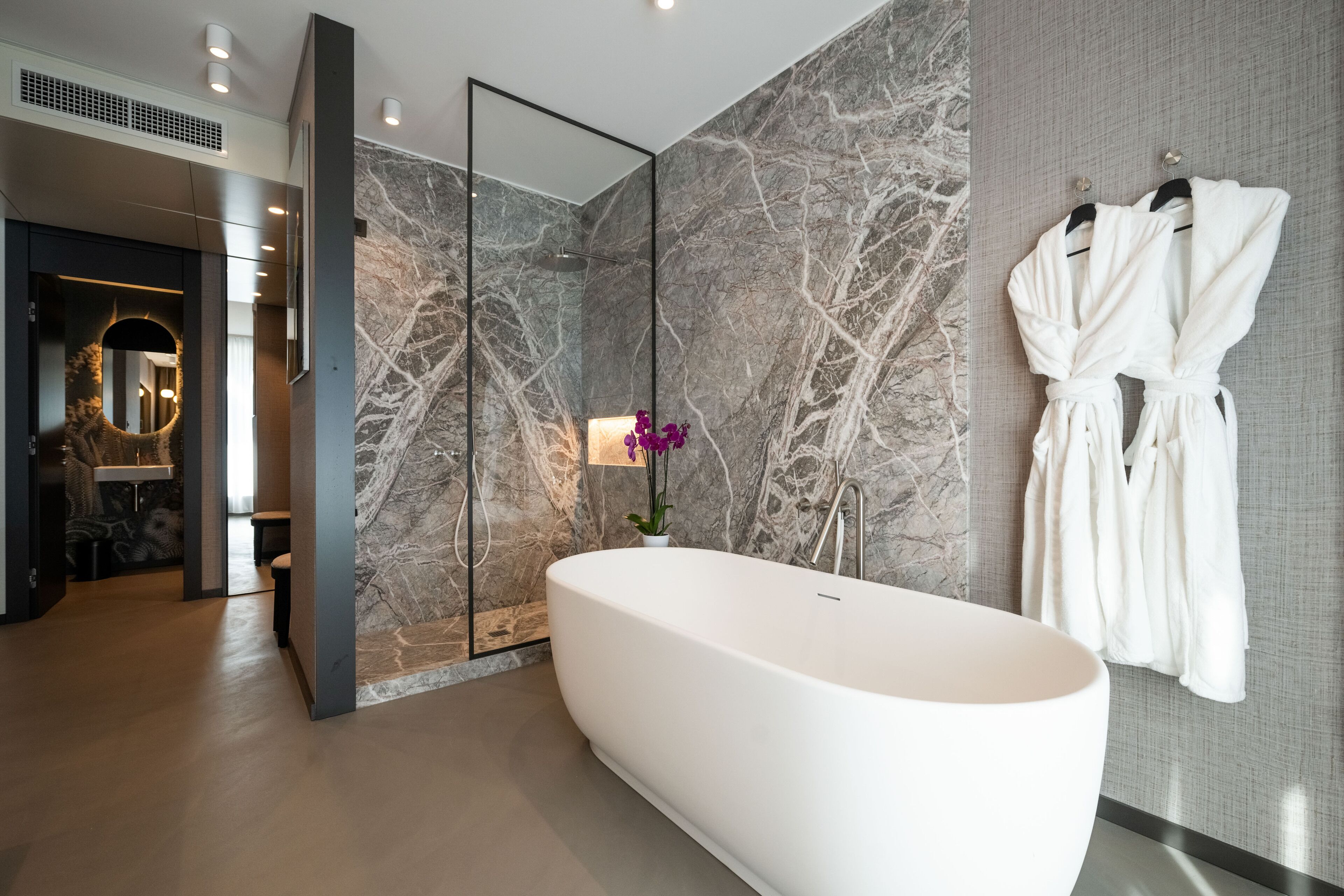 A modern bathroom with a freestanding bathtub, marble walls, and a mirror.