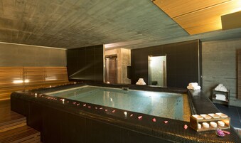 Una spa moderna con una ampia vasca idromassaggio, panche in legno e un pavimento piastrellato.