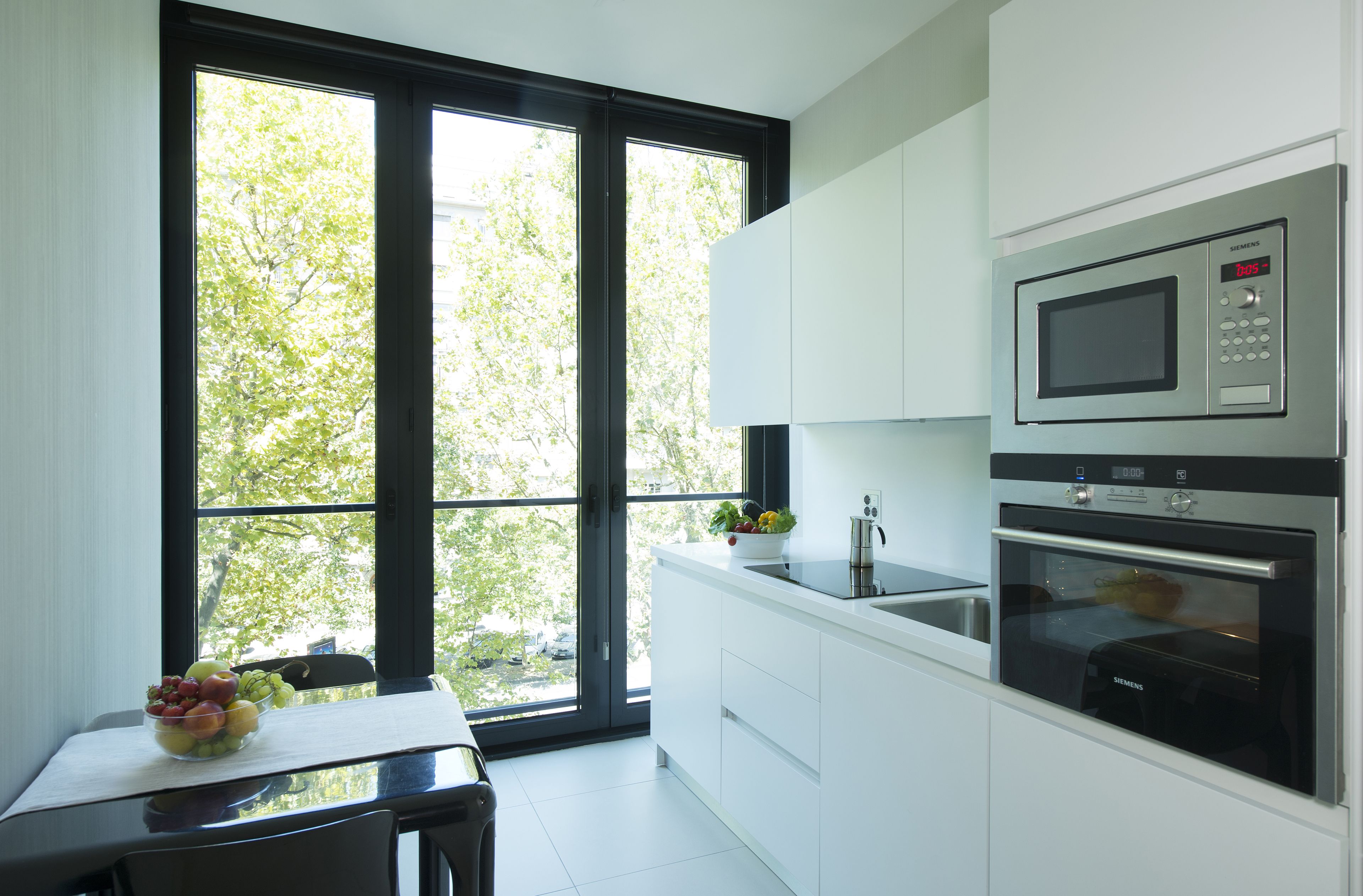 Una cucina moderna con un'ampia finestra, mobili bianchi e un forno a microonde Siemens.
