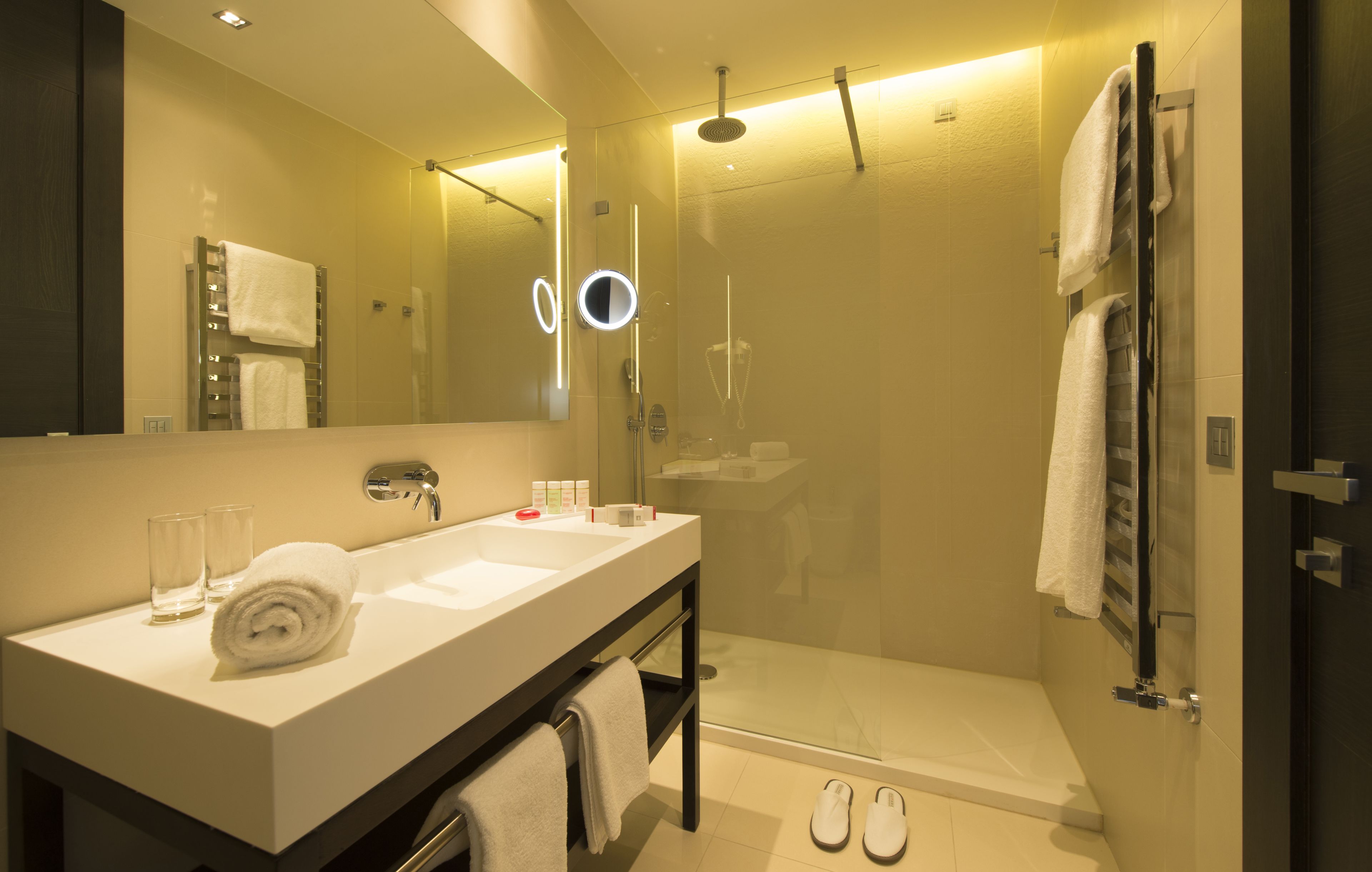 Un bagno moderno con uno specchio grande, un lavandino, una doccia e un paio di ciabatte sul pavimento.