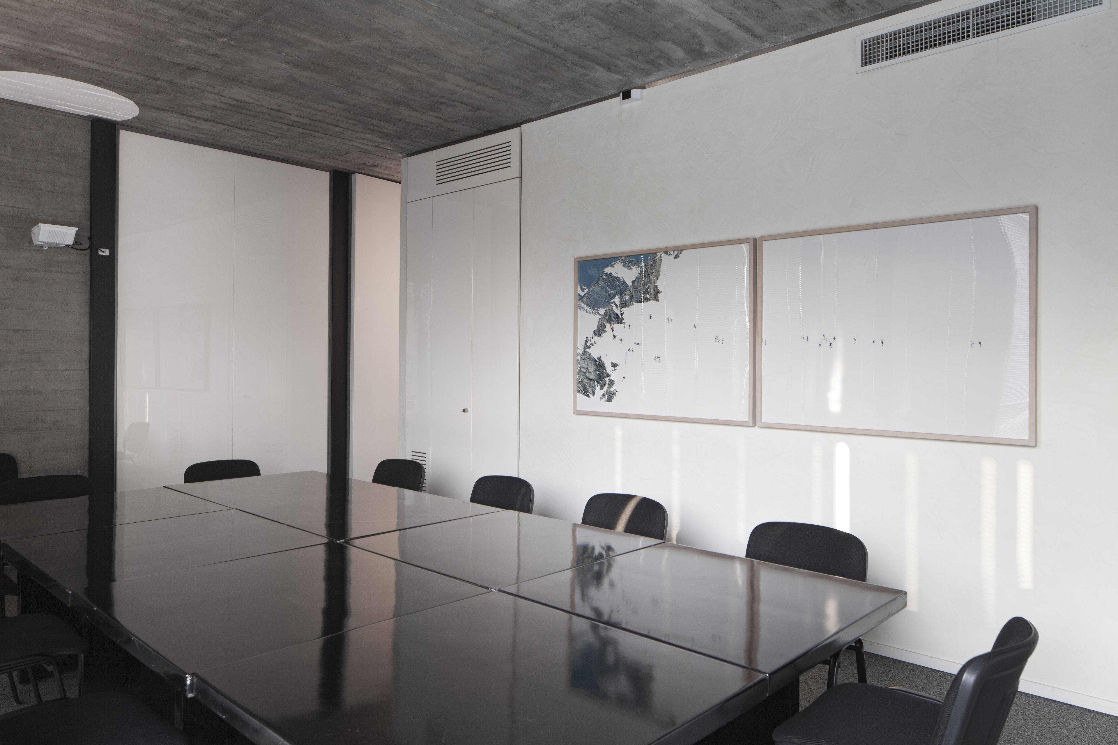 A conference room with a large glass table, six chairs, white walls, and a framed artwork.