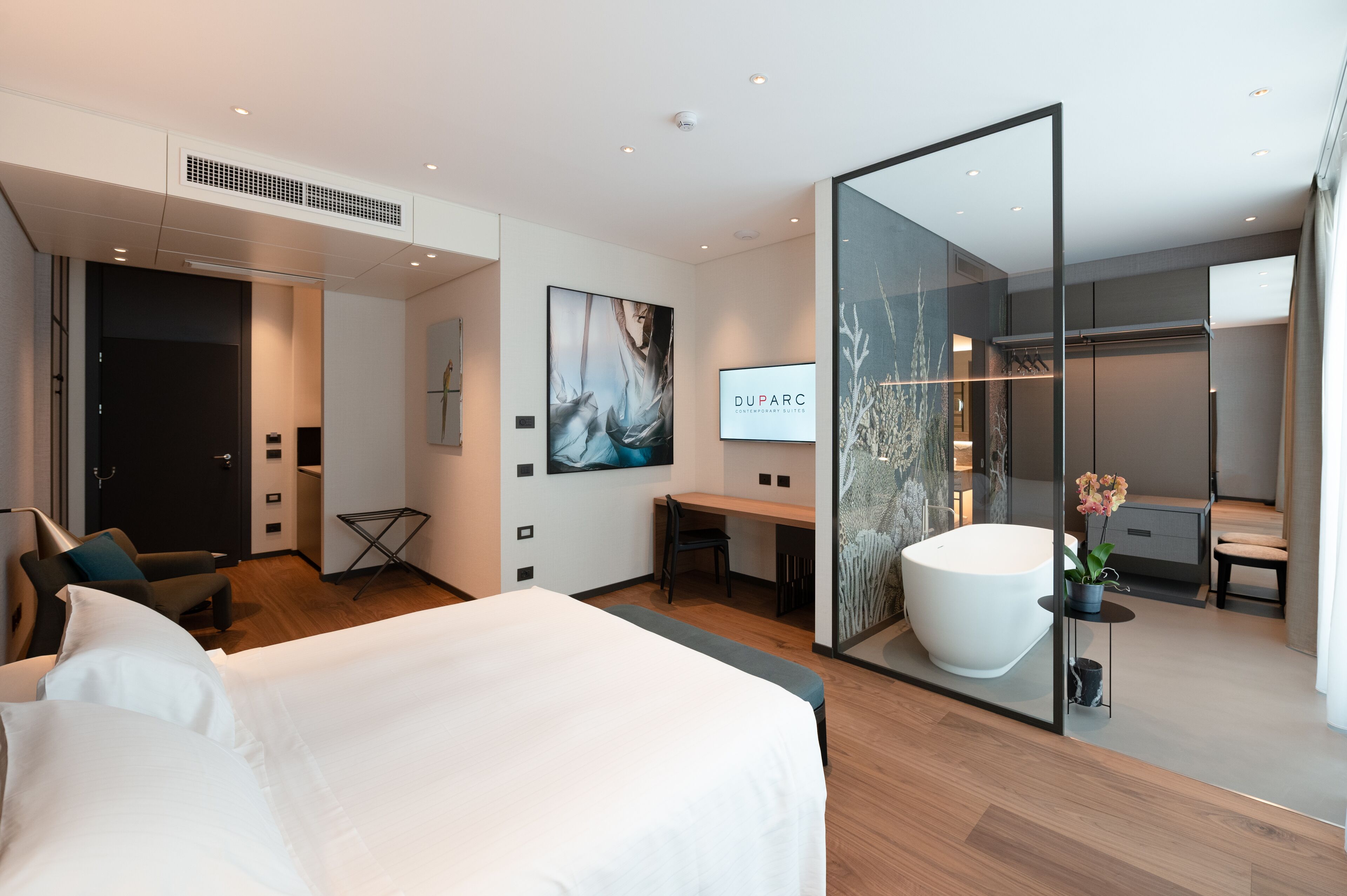 A modern hotel room with a large bed, a desk, a bathtub, and a walk-in closet.