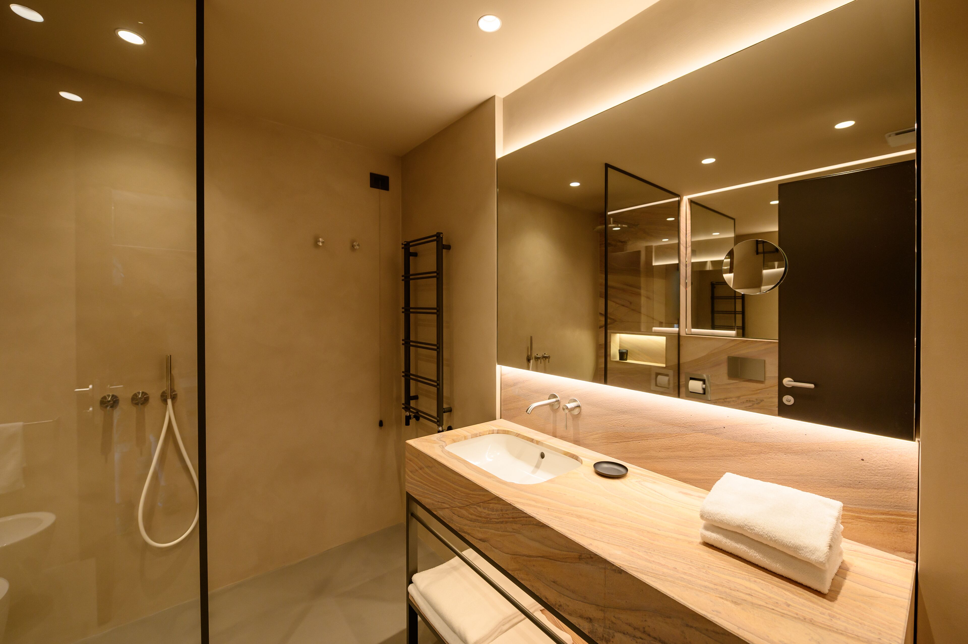 Un baño moderno con cabina de ducha de vidrio, tocador de madera con lavamanos y un espejo grande.