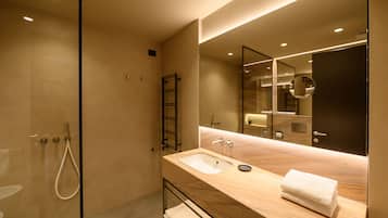 Un baño moderno con cabina de ducha de vidrio, tocador de madera con lavamanos y un espejo grande.
