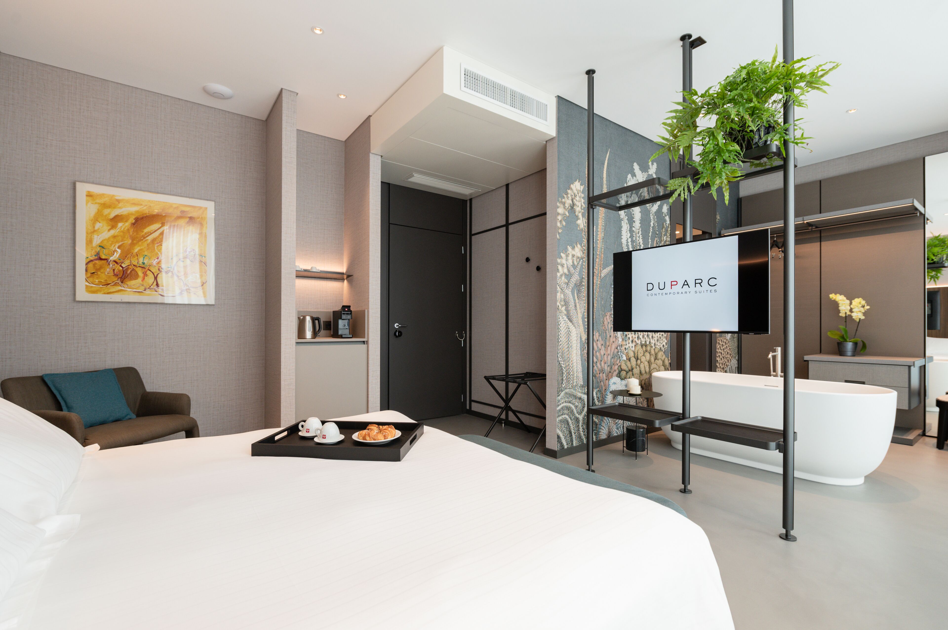 Una habitación de hotel moderna con una cama grande, un sofá, un televisor, una bañera y un comedor con una bandeja de comida.