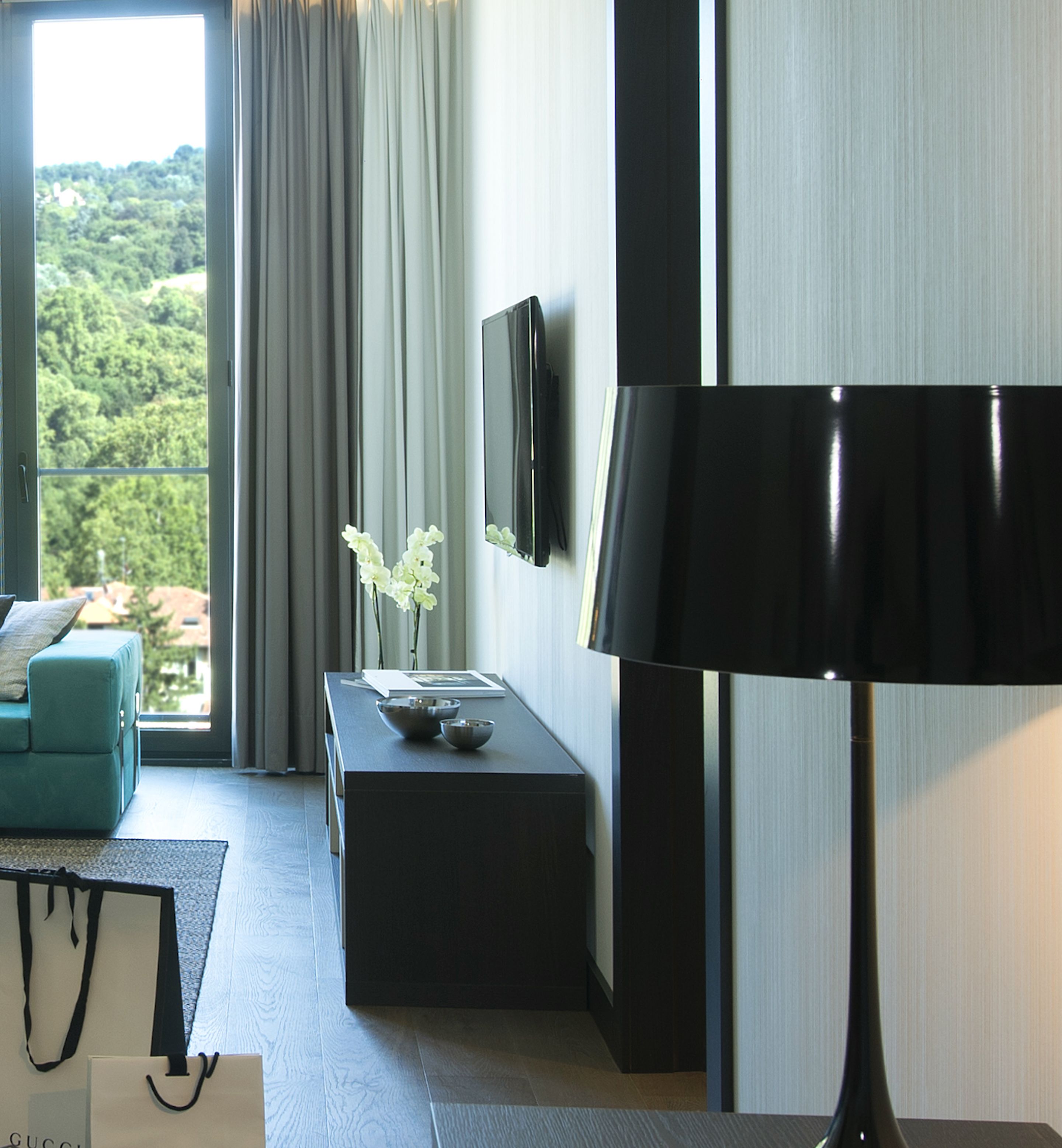 Ein modernes Hotelzimmer mit einer Sitzecke, einem Beistelltisch mit Blumen und einem LCD-Fernseher an der Wand, sowie einer großen Stehlampe.