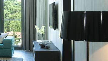 Ein modernes Hotelzimmer mit einer Sitzecke, einem Beistelltisch mit Blumen und einem LCD-Fernseher an der Wand, sowie einer großen Stehlampe.