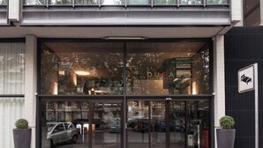 Un edificio moderno con una amplia entrada de vidrio, un cartel que dice "DUPA CONTEMPORARY ART" y dos macetas con plantas en la acera.