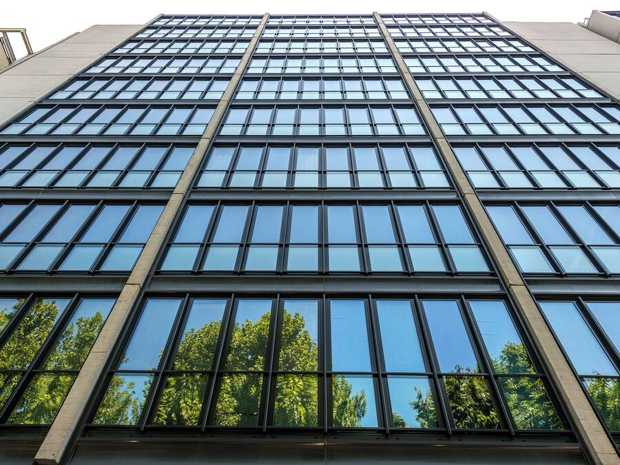 A modern building with a grid of windows and a visible tree line in the background.
