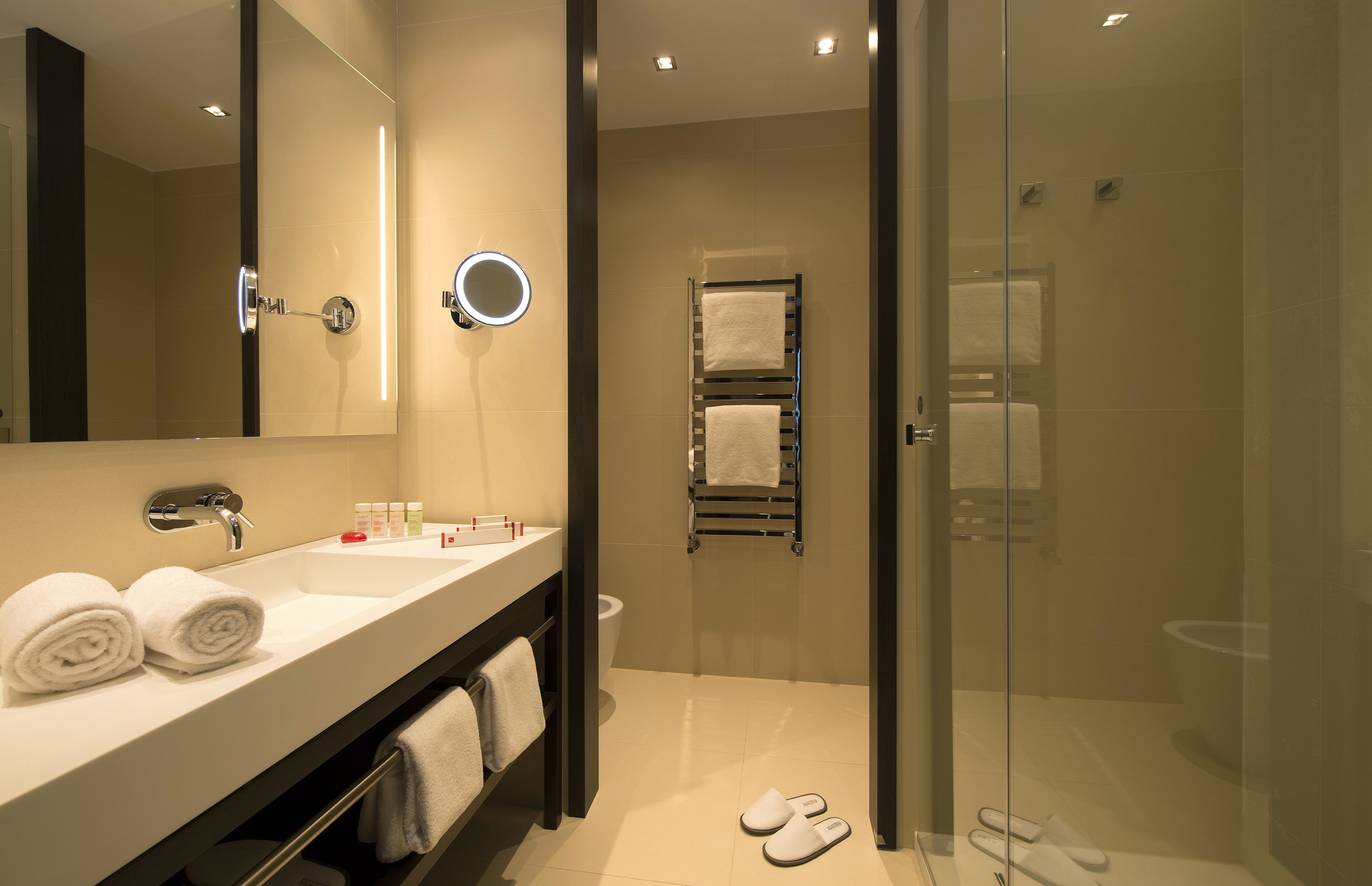 A modern bathroom with a glass-enclosed shower, a large mirror, and a vanity with toiletries.