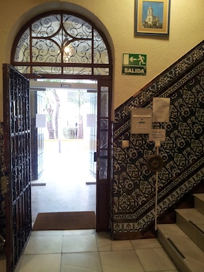 An entrance with a wrought iron gate, a sign indicating the exit, and a staircase with patterned tiles. - Pensión Catedral (Seville)