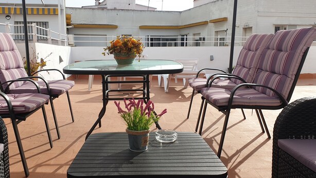A rooftop terrace with a glass table surrounded by striped chairs, a potted plant, and a clear ashtray. - Pensión Catedral (Seville)